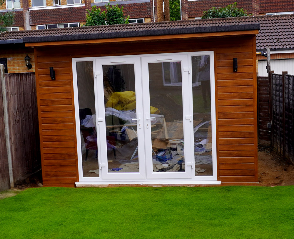 Timber-clad garden office with white French doors and finished lawn