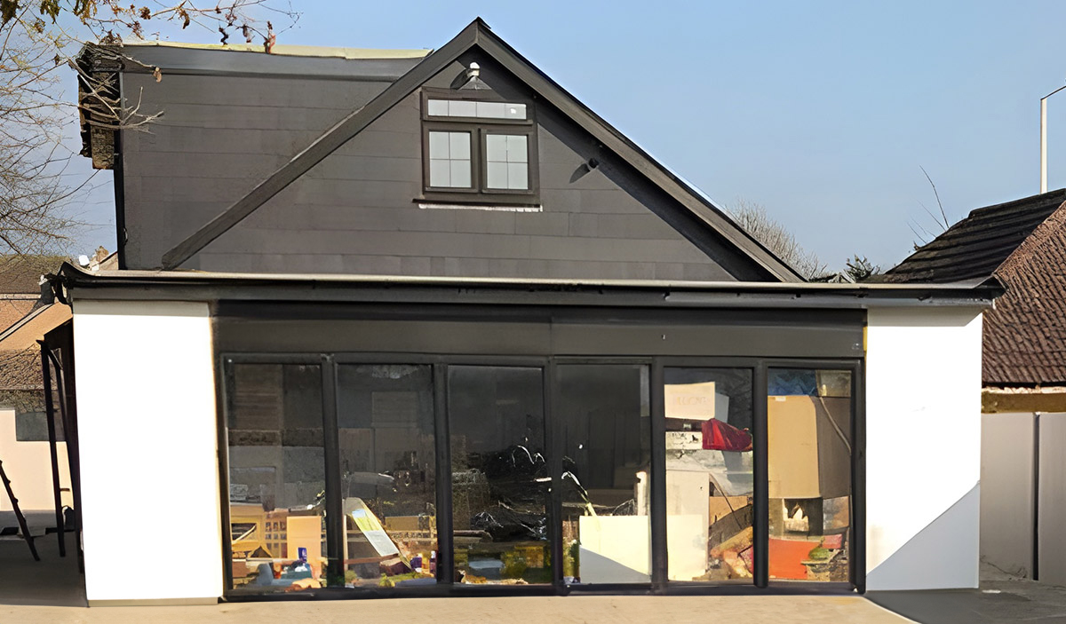 Exterior of the extended house with glazed doors, white walls and dark gable cladding