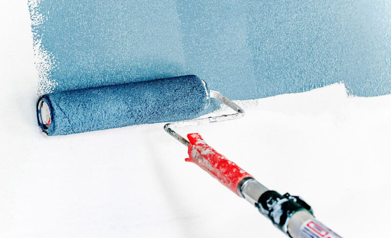 Paint roller applying blue paint to a white wall
